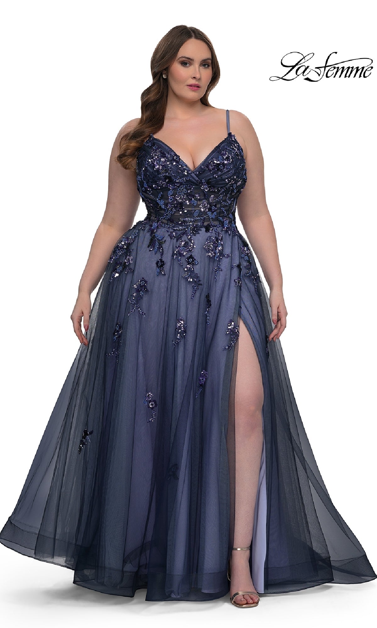 A woman wears the Navy Plus-Size Prom Dress: La Femme 33061, featuring sequin beaded floral appliqué, a deep V-neckline, spaghetti straps, an A-line skirt, and a high slit, standing against a plain white background.